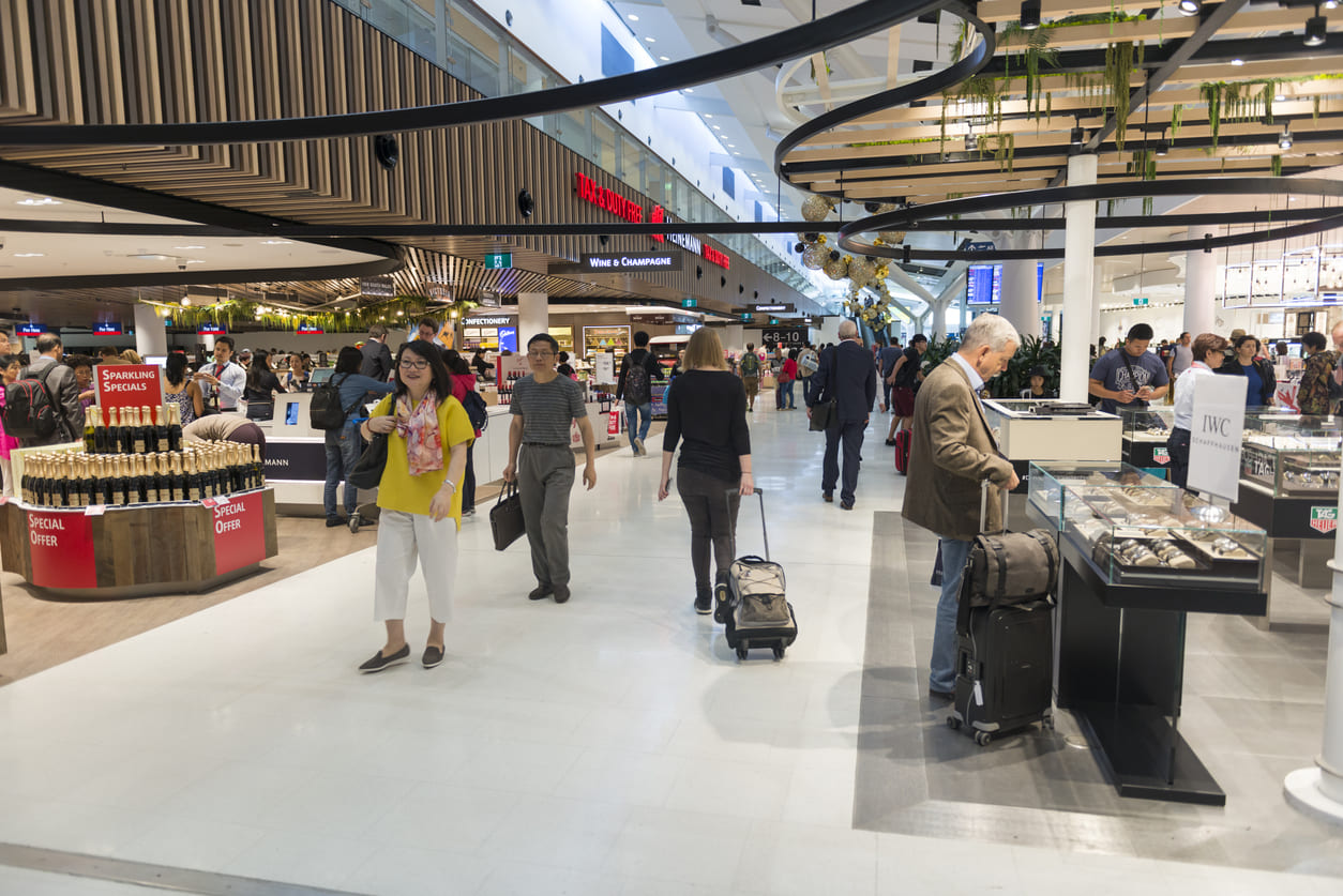 Passengers exploring the lively duty-free shopping area at Sydney Airport, surrounded by luxury goods and vibrant retail displays.