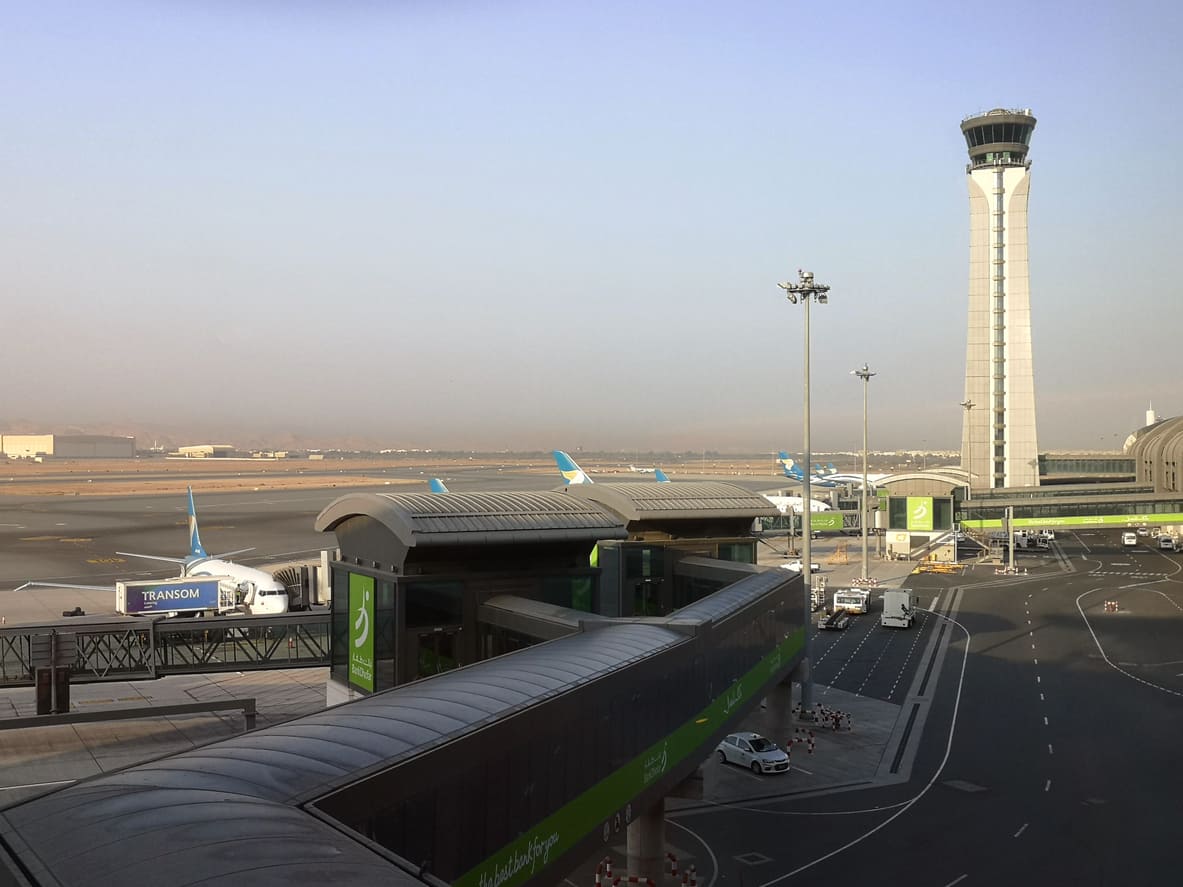 The modern infrastructure of Muscat International Airport, featuring its iconic control tower and Oman Air aircraft on the tarmac.