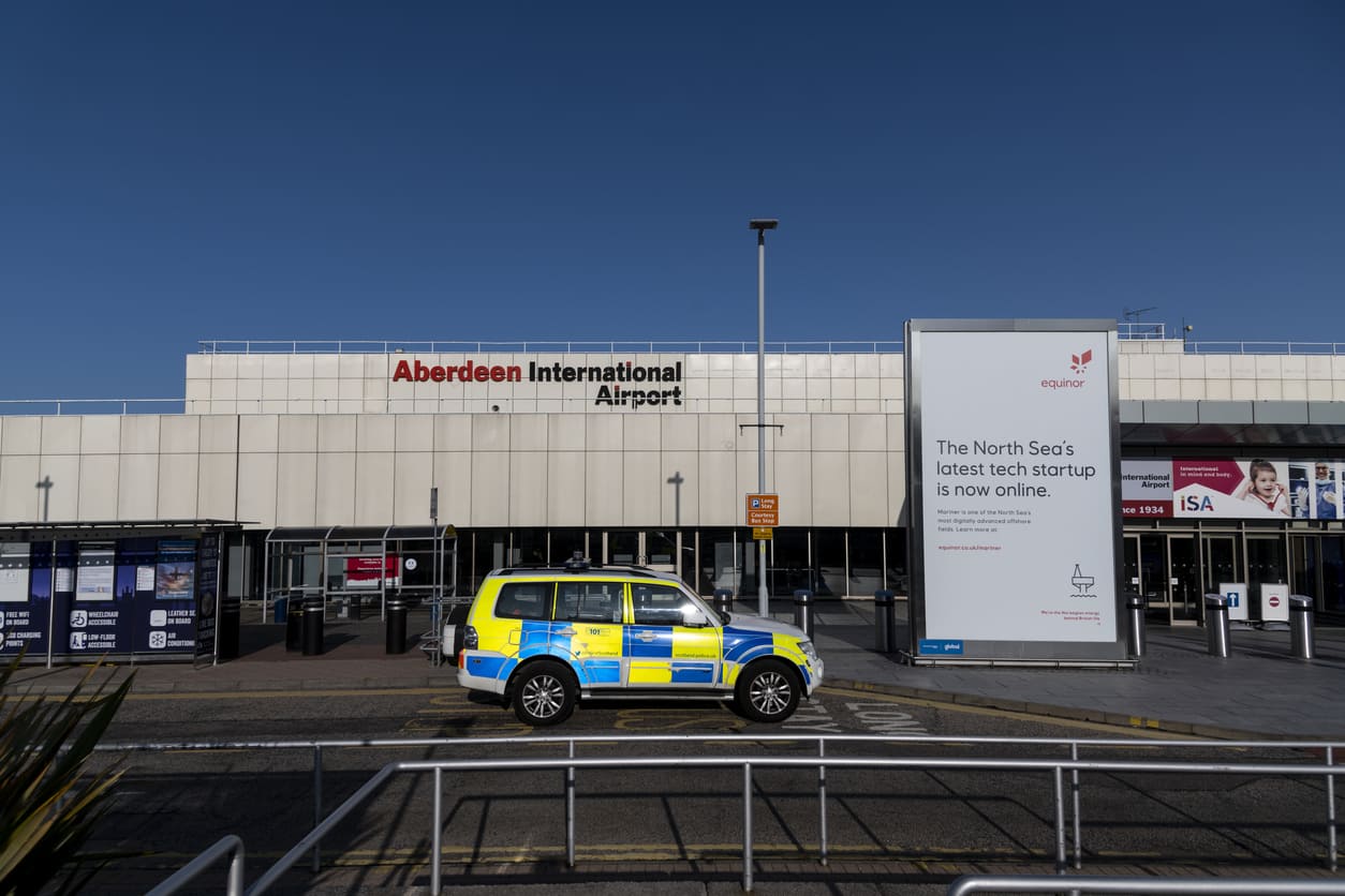 The exterior of Aberdeen International Airport displays a clean, modern design with prominent signage under a clear blue sky.