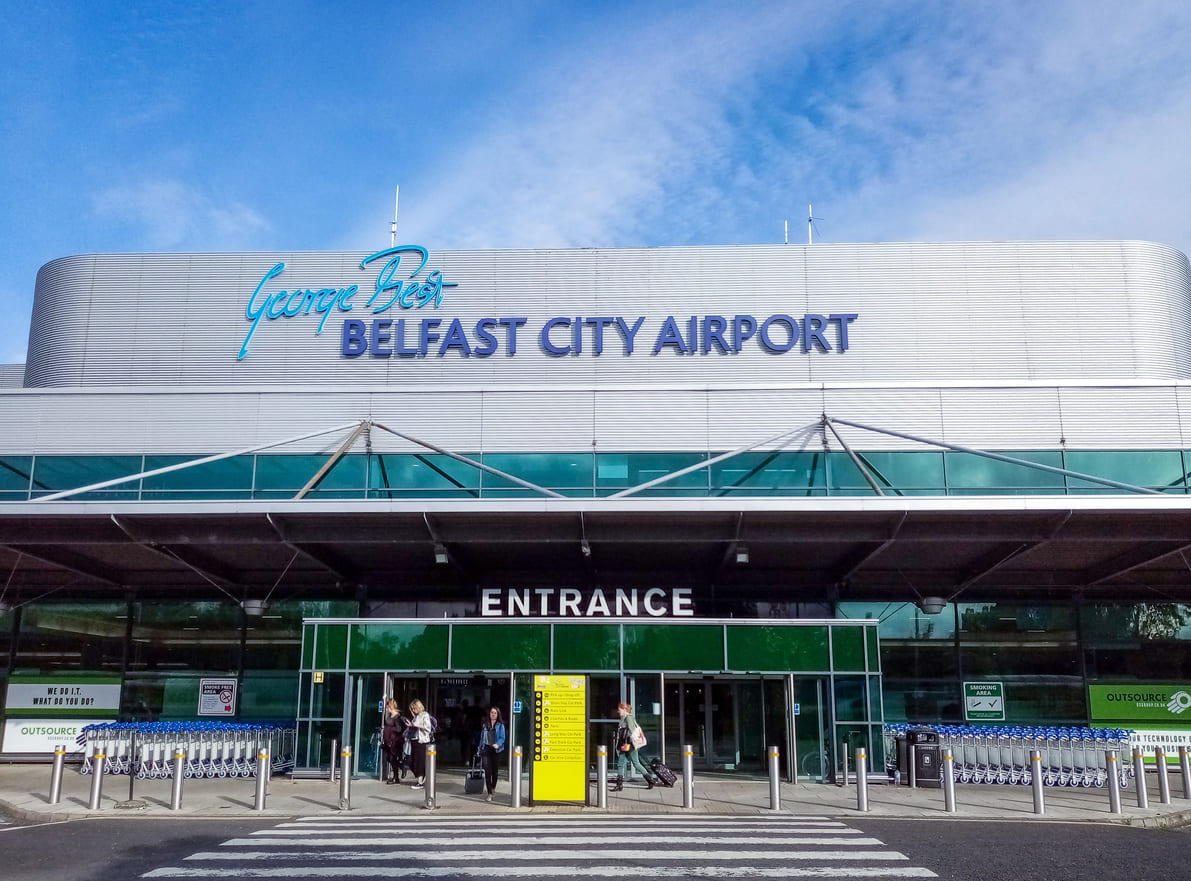 The entrance of George Best Belfast City Airport displays sleek architecture with prominent signage, creating a welcoming atmosphere for travelers.