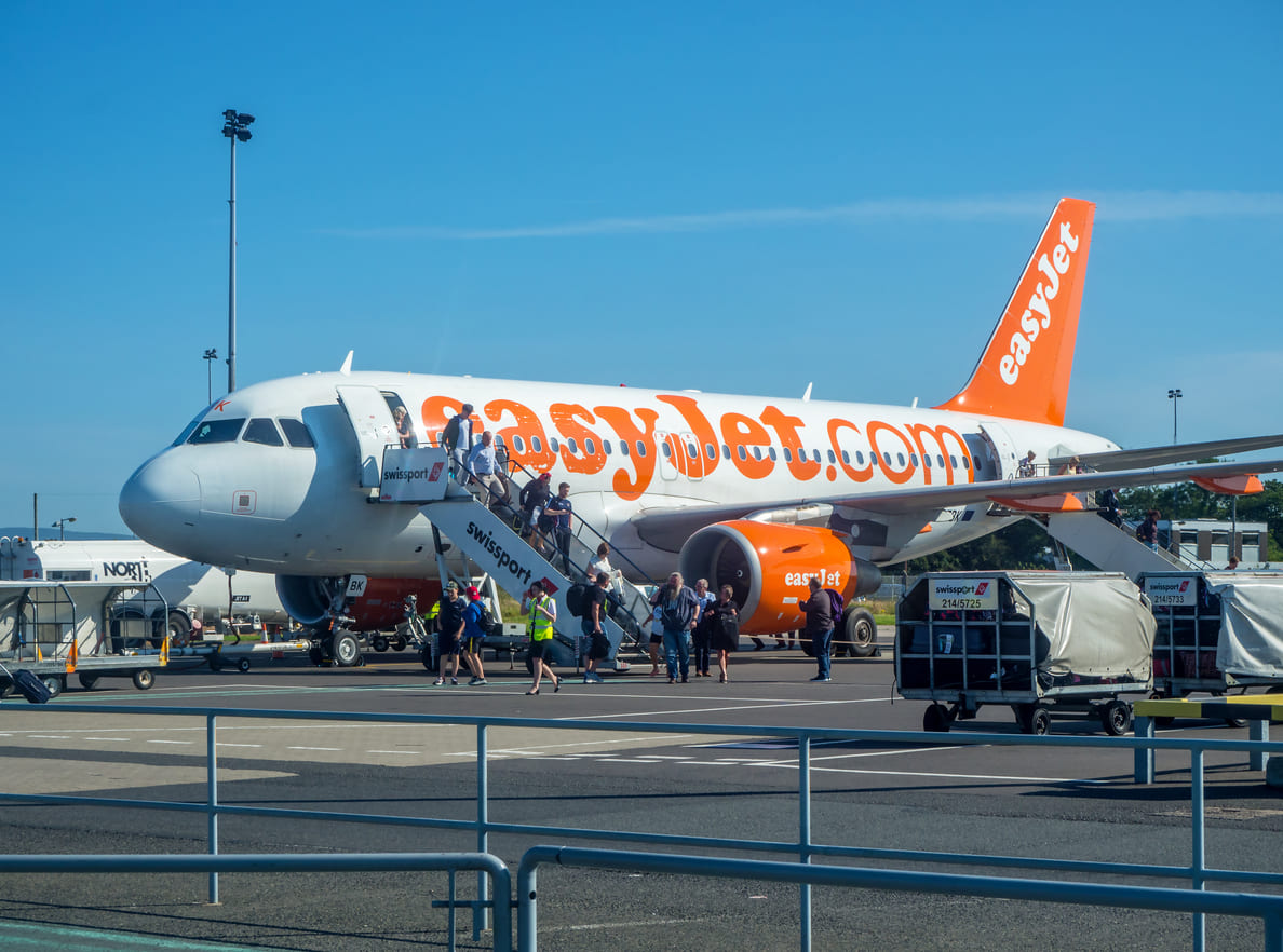 Passengers are seen disembarking from an easyJet aircraft at Belfast International Airport on a sunny day.