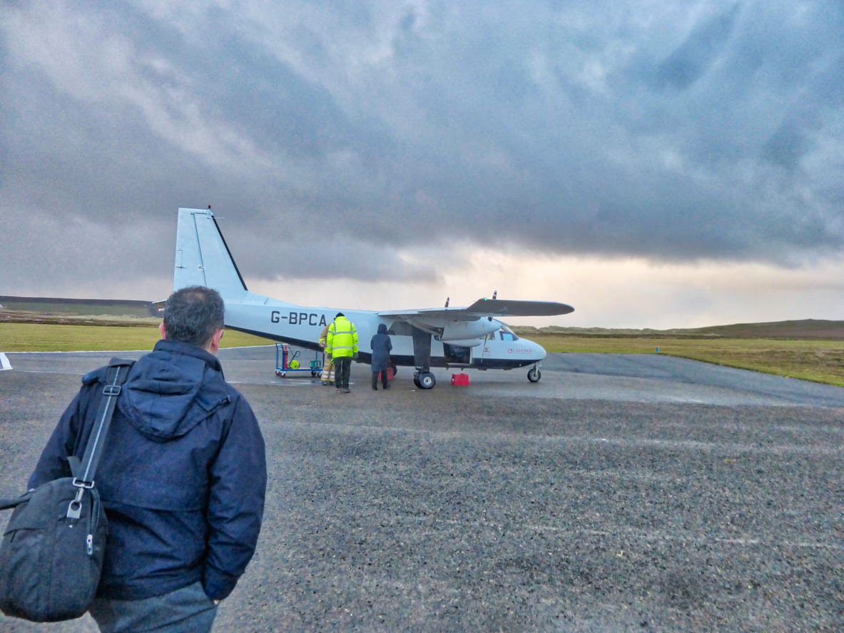 A passenger prepares to board a small Loganair aircraft at Eday Airport under dramatic skies.