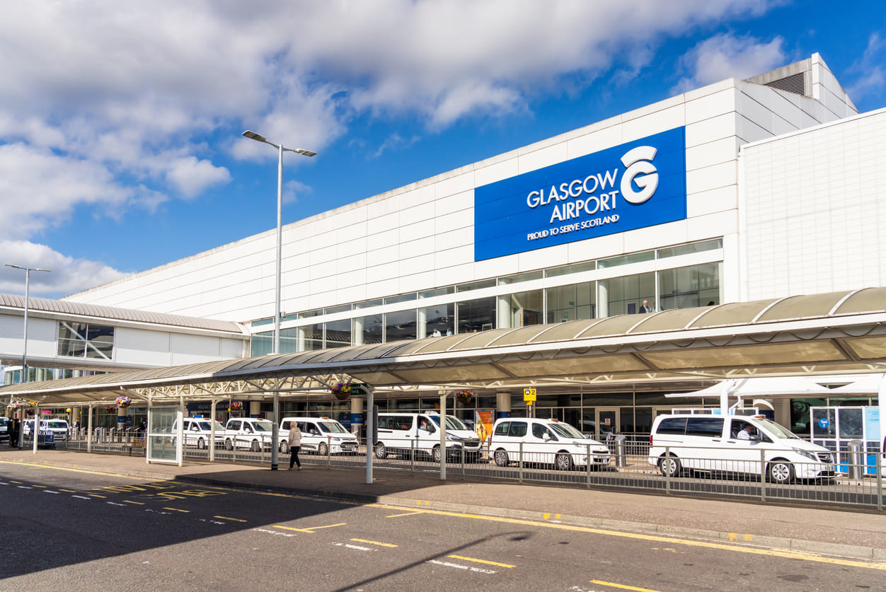 The exterior of Glasgow Airport, showcasing its sleek design, clear signage, and a busy drop-off area with vehicles and passengers.