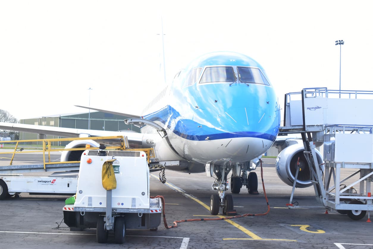 A blue-and-white aircraft is parked on the tarmac, connected to ground handling equipment for servicing.