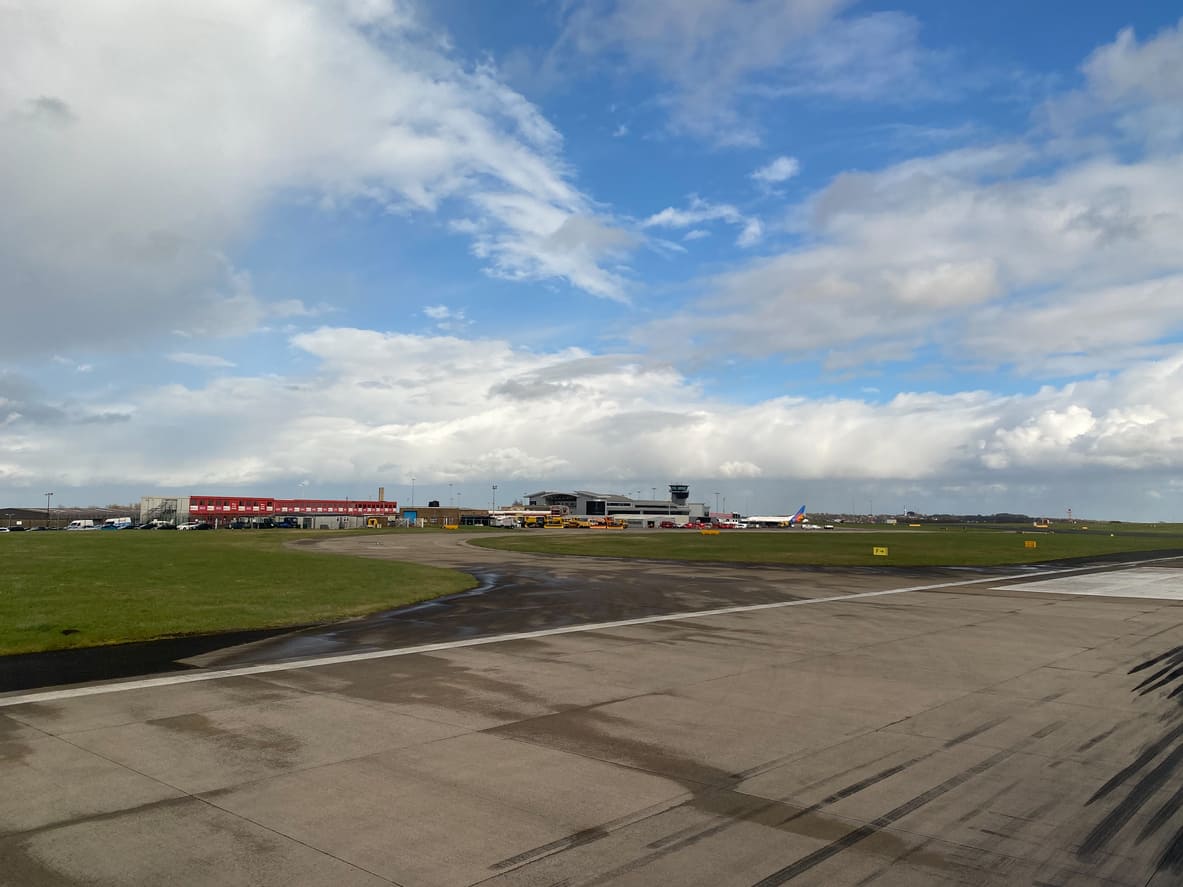 Leeds Bradford Airport's runway and terminal are surrounded by green fields, with a clear, expansive sky overhead.