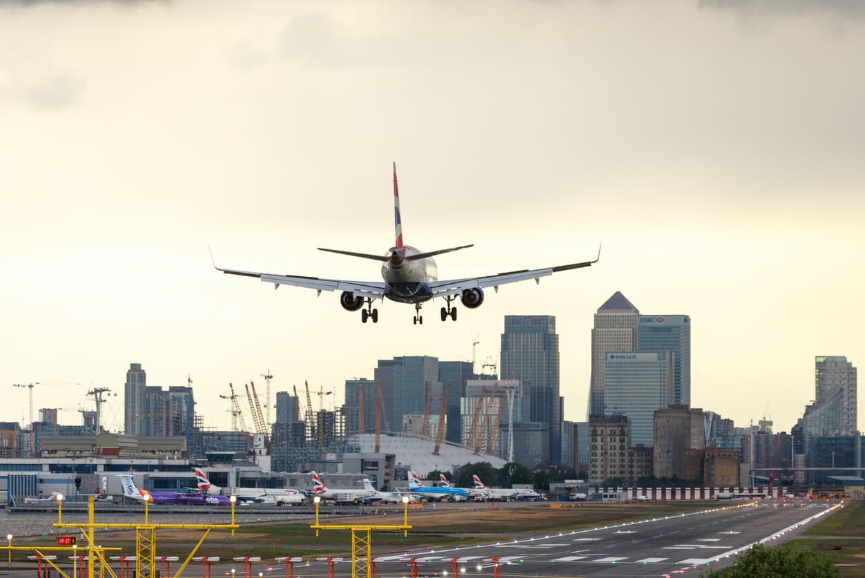 A plane is seen landing at London City Airport with the striking skyline of Canary Wharf in the background.