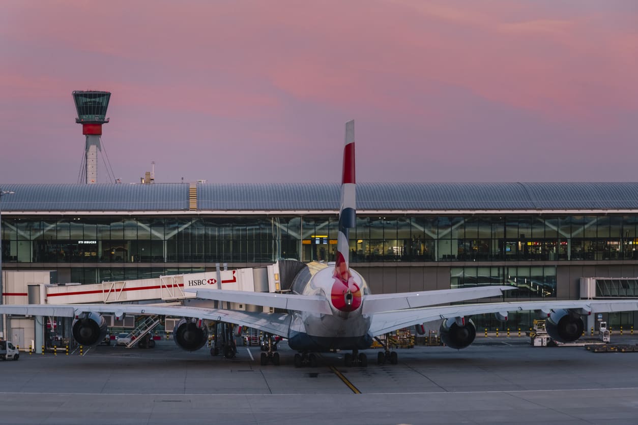 A British Airways plane at London Heathrow Airport, with the control tower and terminal framed by a serene sunset.