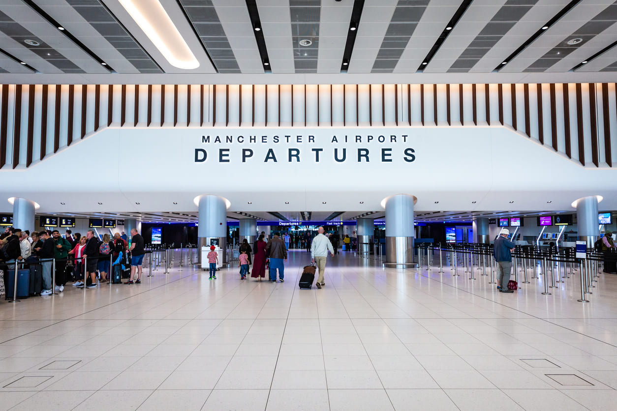 Manchester Airport's departures area showcases a sleek, spacious design with travelers lining up for check-ins and security.