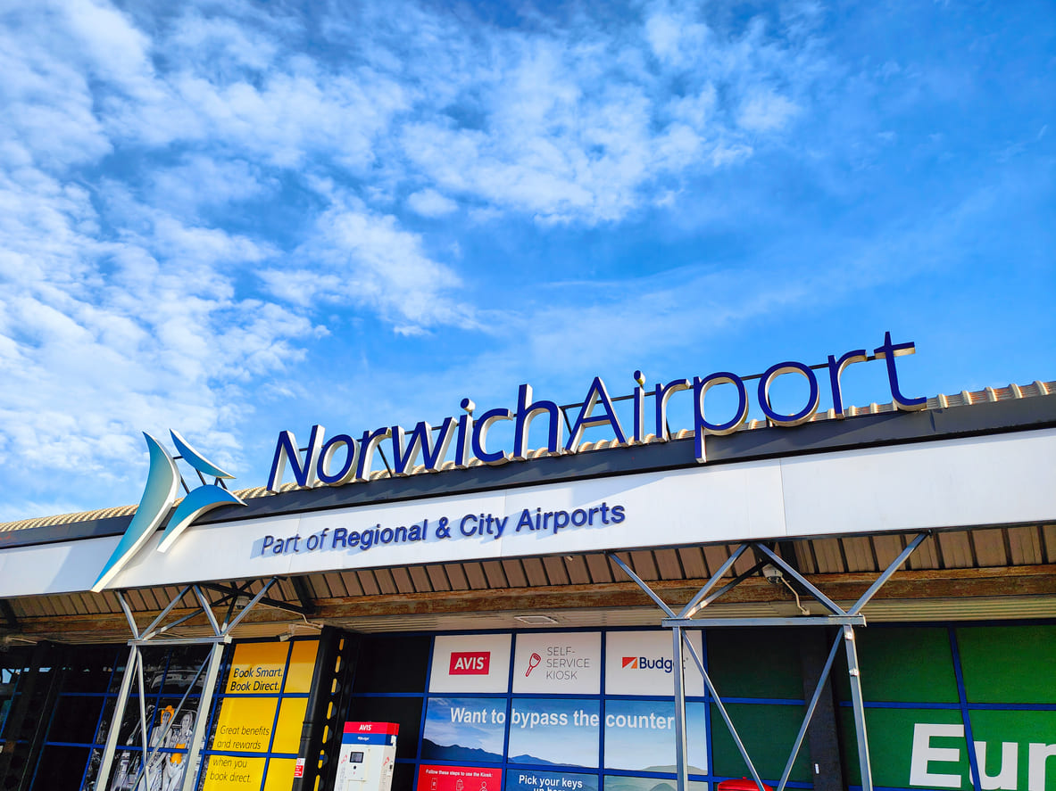 The main entrance of Norwich Airport, featuring its bold signage and clear branding under a bright blue sky.