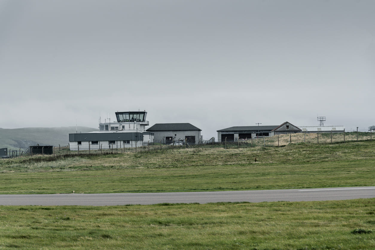 The control tower and surrounding facilities of Sumburgh Airport, nestled in a misty, grassy landscape.