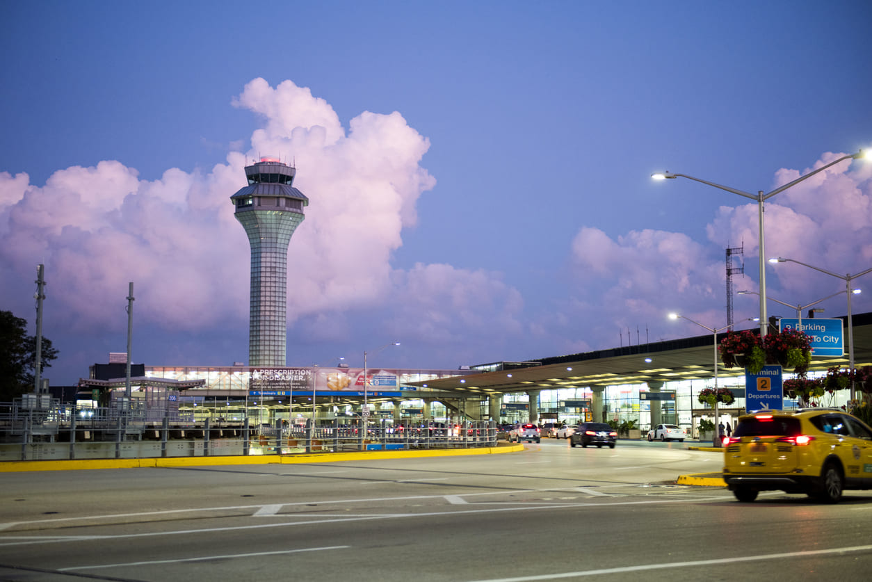 Chicago O'Hare Airport at dusk, with its illuminated control tower, terminal, and active roadway.