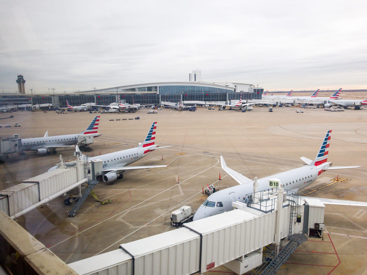 Dallas Fort Worth International Airport with American Airlines planes at the gates, highlighting its busy operations and modern terminal.