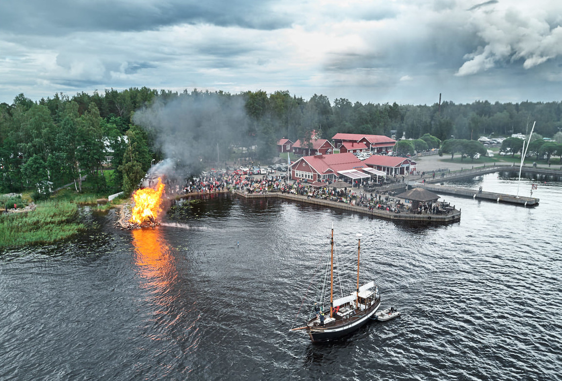 A Midsummer Eve celebration with a lakeside bonfire, crowds, and red cottages, capturing the essence of Finnish summer tradition.