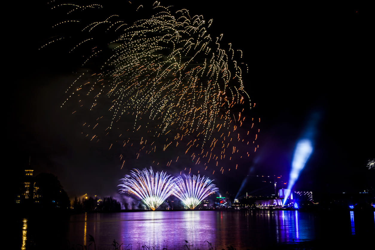 Colorful fireworks explode above Töölönlahti Bay in Helsinki, reflecting on the water as the city celebrates New Year's Day.