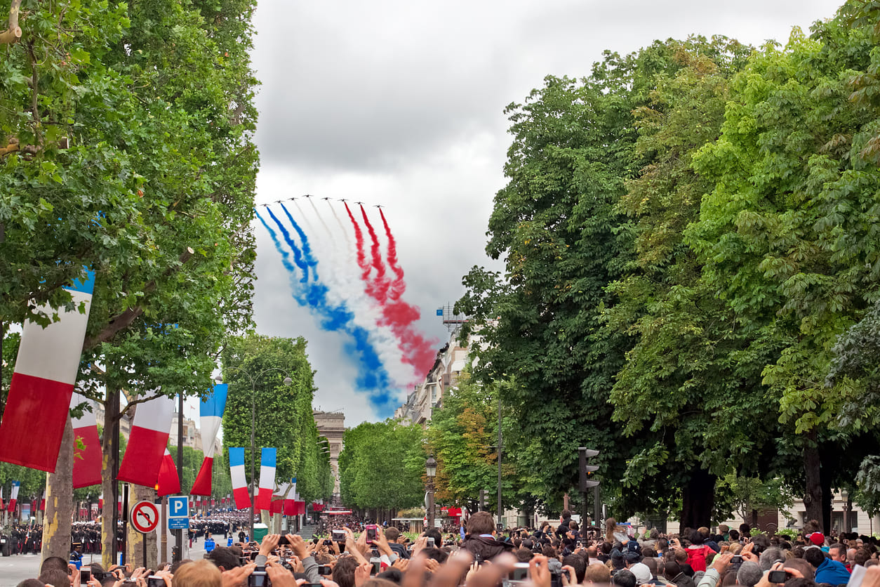 A formation of jets streaks the sky with blue, white, and red as crowds gather on the Champs-Élysées for Bastille Day celebrations.