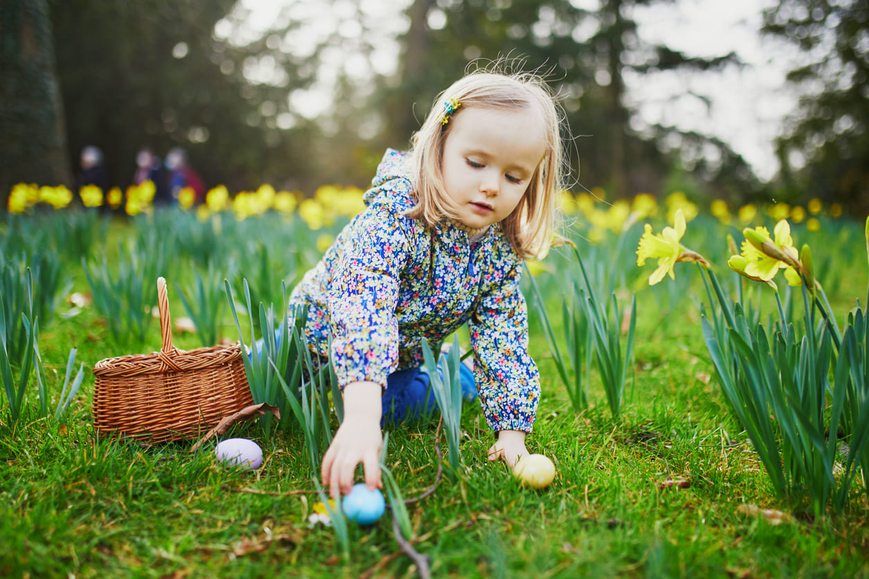 A young girl happily participates in an Easter egg hunt, surrounded by blooming spring flowers.