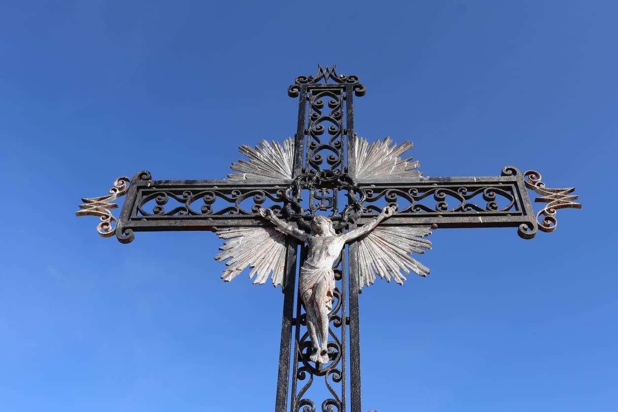 A detailed wrought iron crucifix stands tall against a clear blue sky, symbolizing faith and reflection.