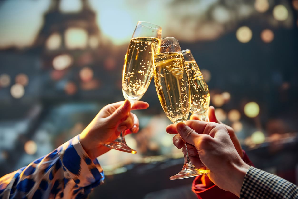 Friends share a champagne toast on New Year's Eve with the Eiffel Tower glowing softly in the background.