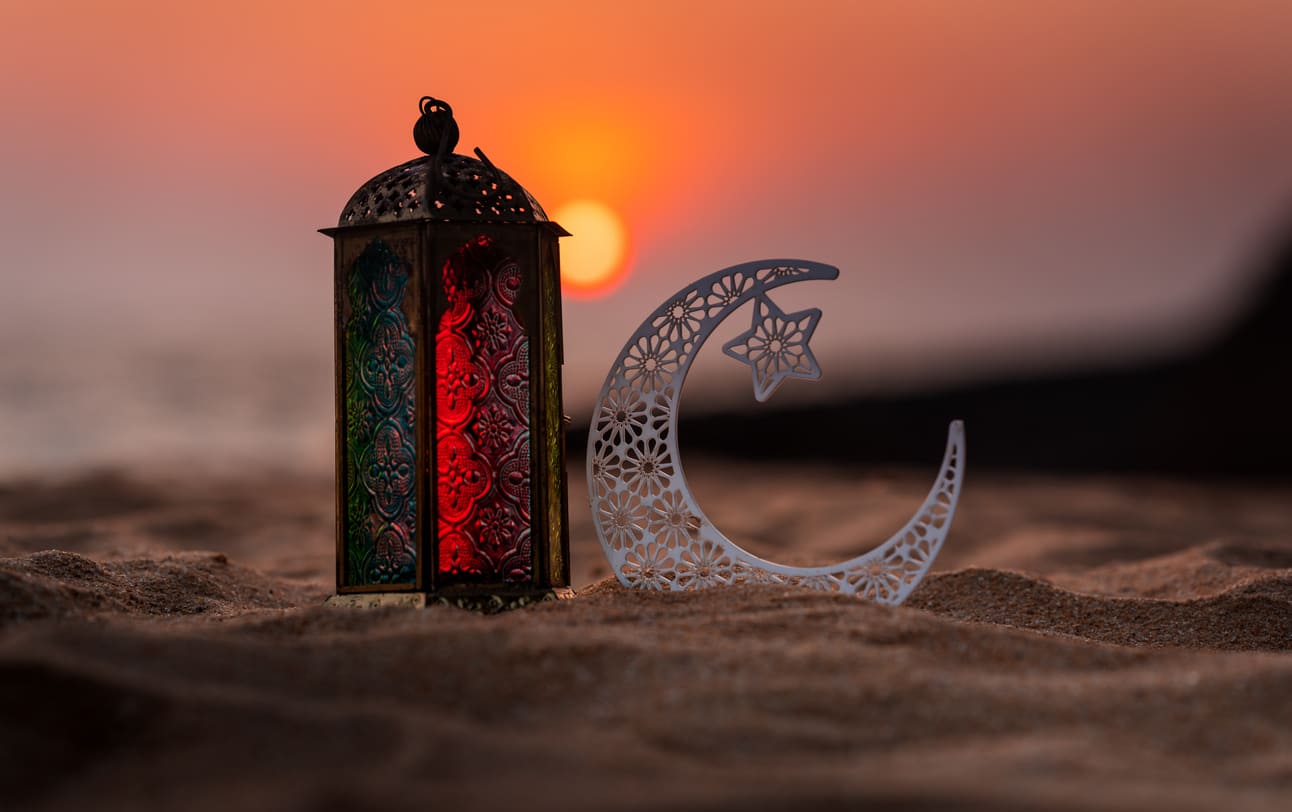 A colorful lantern and crescent moon symbol set against a serene sunset, symbolizing the beginning of Ramadan.