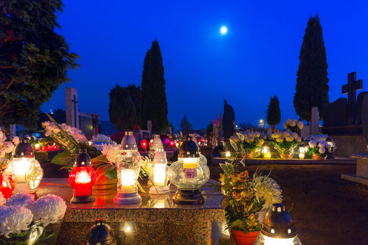 Graves beautifully lit with candles and decorated with flowers, creating a tranquil and reflective scene under a moonlit sky.