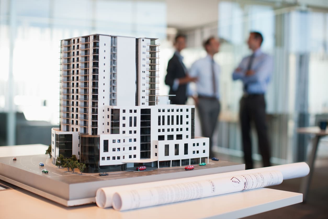 An architectural model of a modern building with professionals discussing in the background.