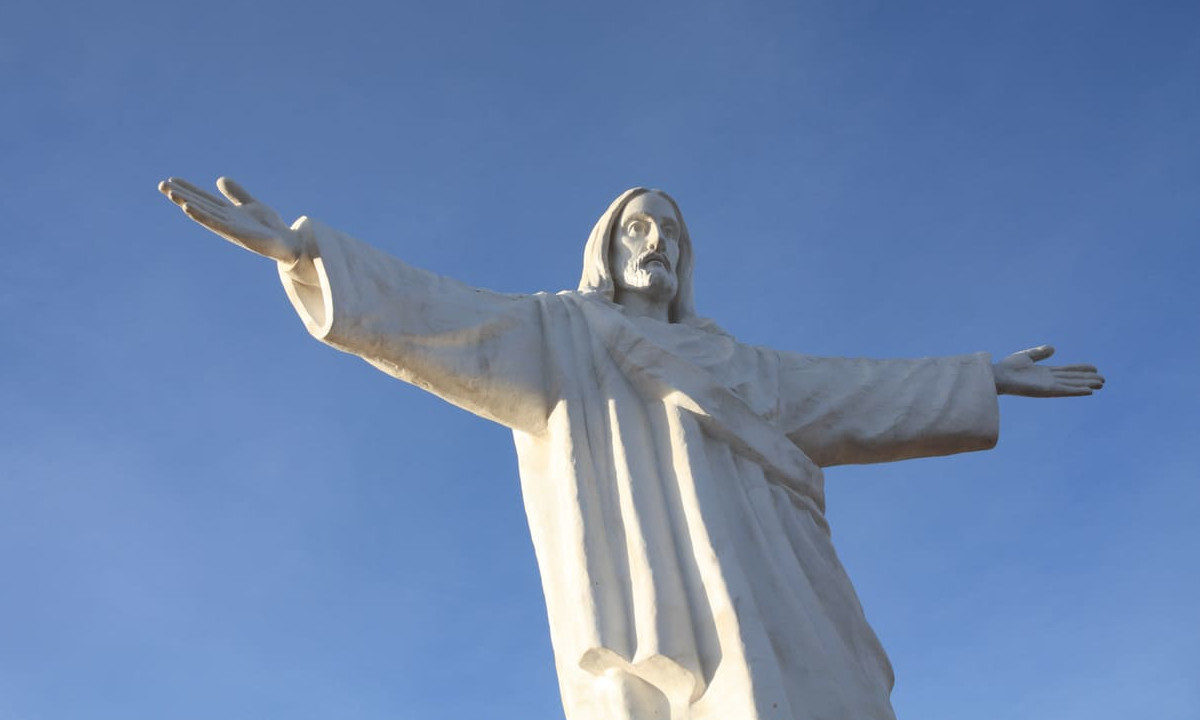 A majestic statue of Jesus Christ with outstretched arms, set against a clear blue sky, symbolizing ascension and divine grace.