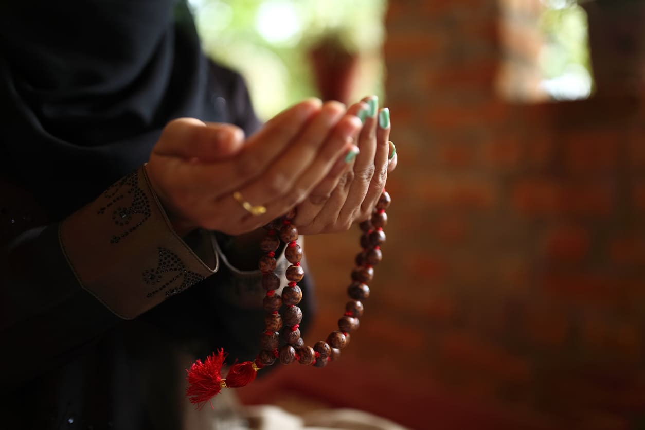 A person holding prayer beads with hands raised in supplication, reflecting a moment of spiritual devotion.