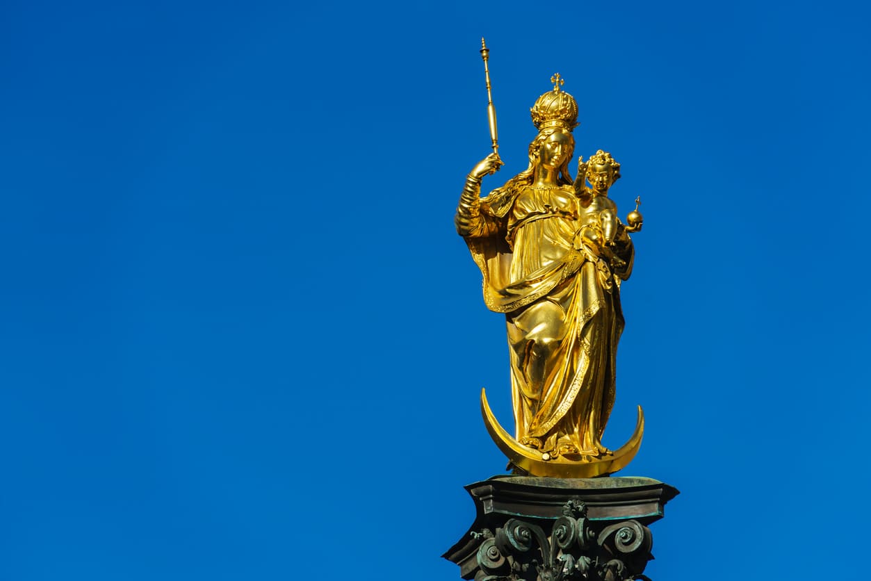 A golden statue of the Virgin Mary and Child stands gracefully against a vibrant blue sky, symbolizing faith and devotion.