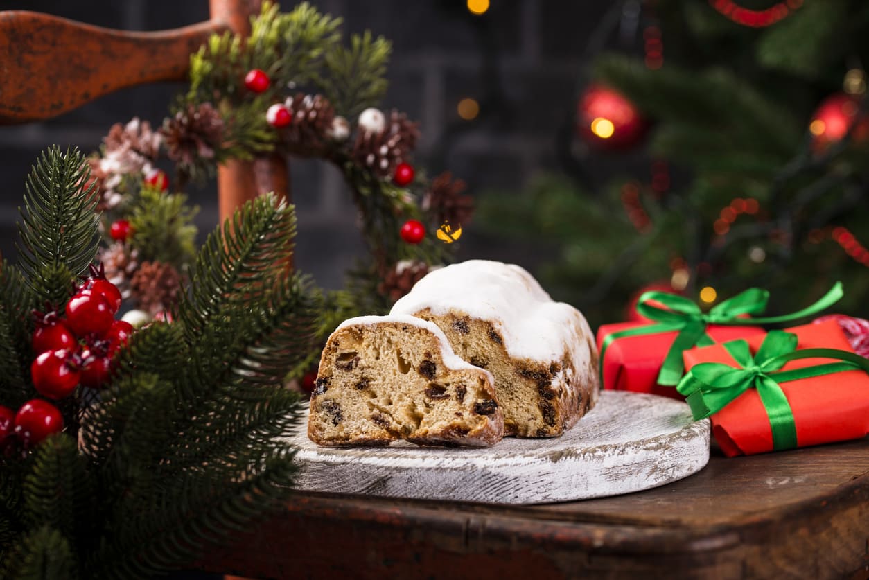 A festive German Stollen, dusted with powdered sugar, sits on a holiday-decorated table alongside wrapped gifts and Christmas greenery.