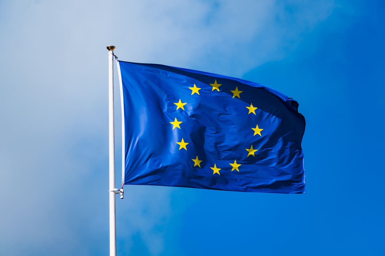 A vibrant European Union flag with golden stars waves against a clear blue sky.