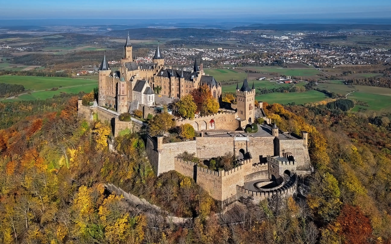 Hohenzollern Castle perched atop a hill, surrounded by autumn foliage.