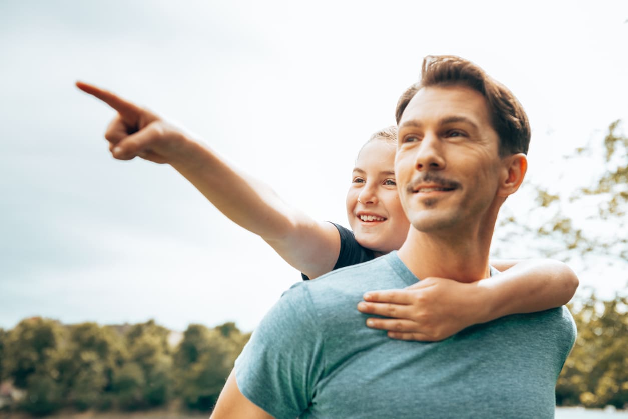 A father carries his smiling child on his back as they enjoy a moment of exploration and bonding outdoors.