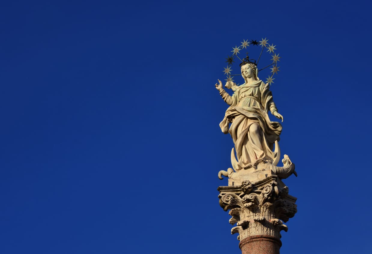 A statue of the Virgin Mary crowned with stars stands gracefully atop a column, symbolizing her purity and the reverence of the Feast of the Immaculate Conception.