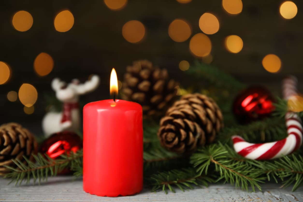 A red candle burning on an Advent wreath, surrounded by festive decorations, symbolizes the start of the Advent season.