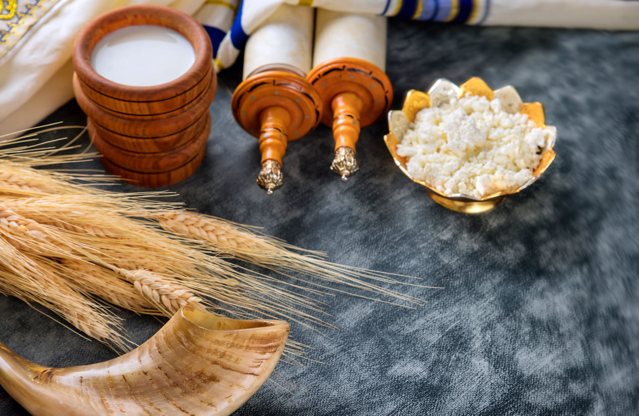 Torah scrolls, dairy foods, wheat, and a shofar, symbolizing the traditions and significance of Shavuot.