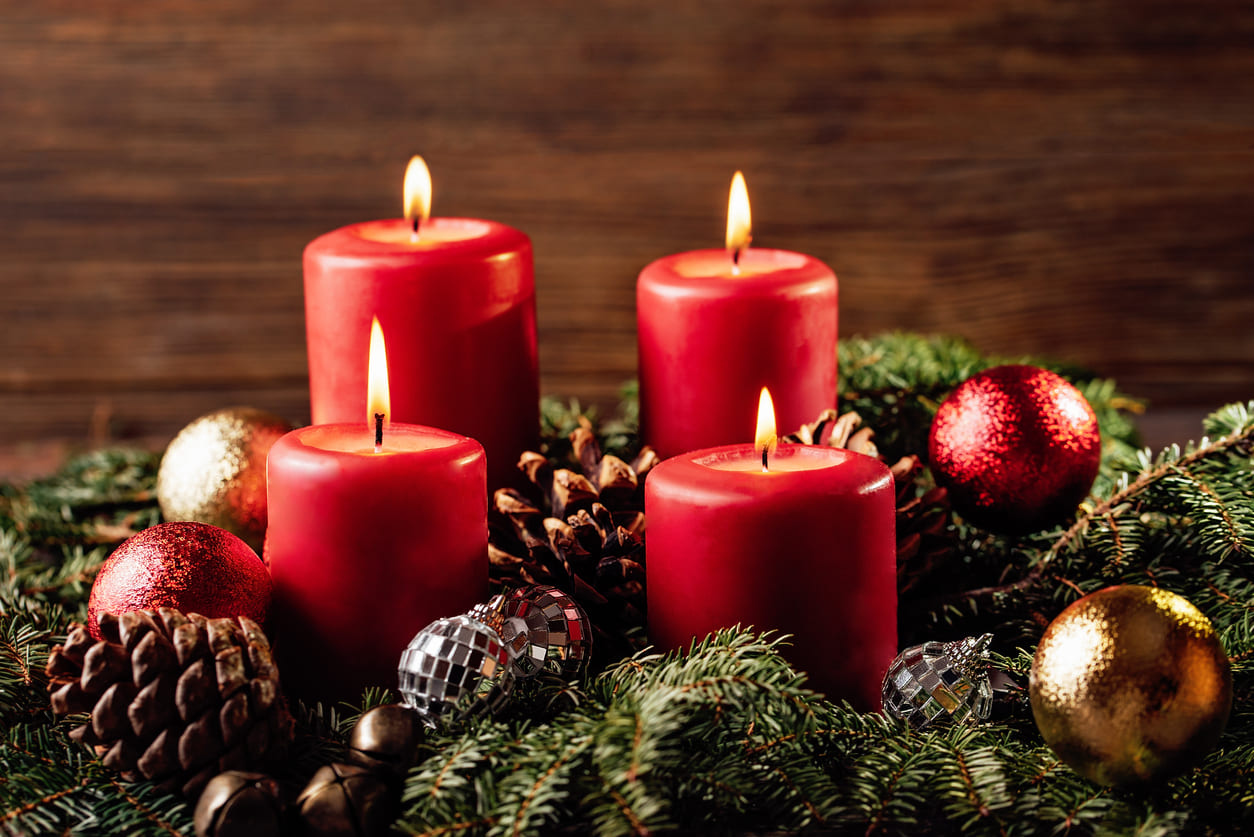 Four red candles glowing on an Advent wreath, representing the Fourth Advent Sunday.