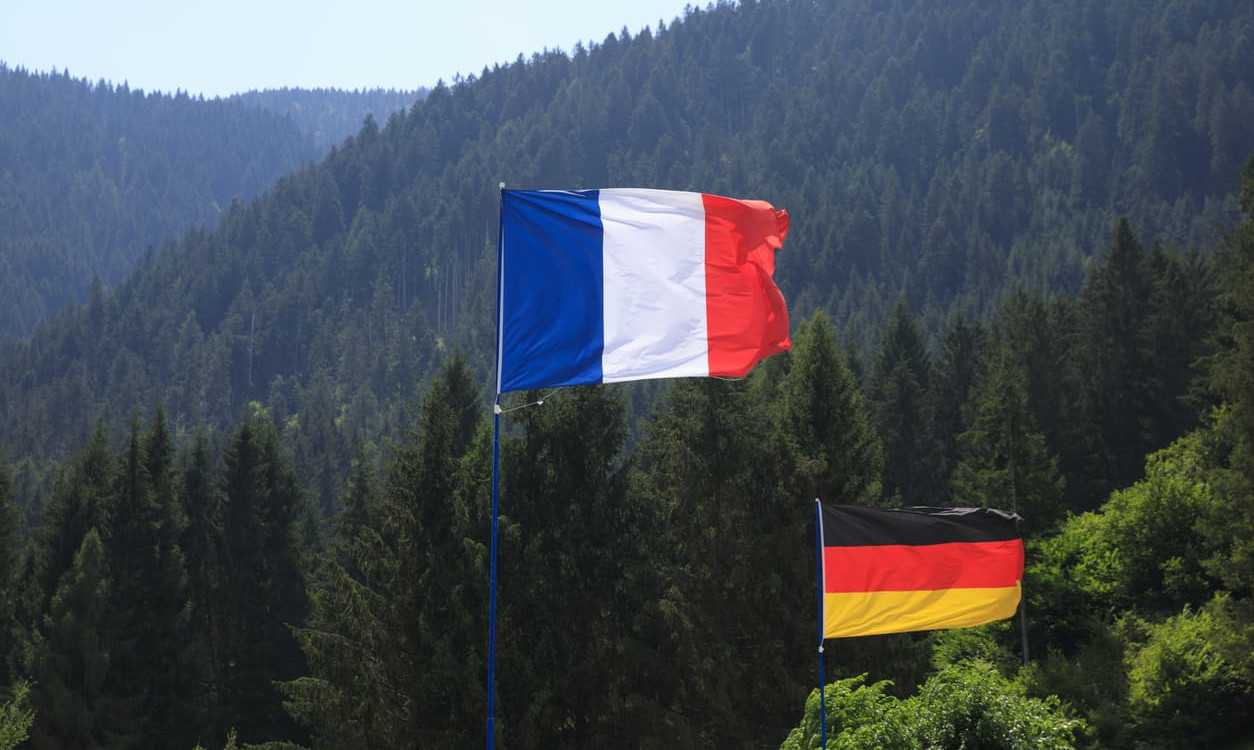 The French and German flags stand side by side against a lush green forest, symbolizing harmony and partnership.