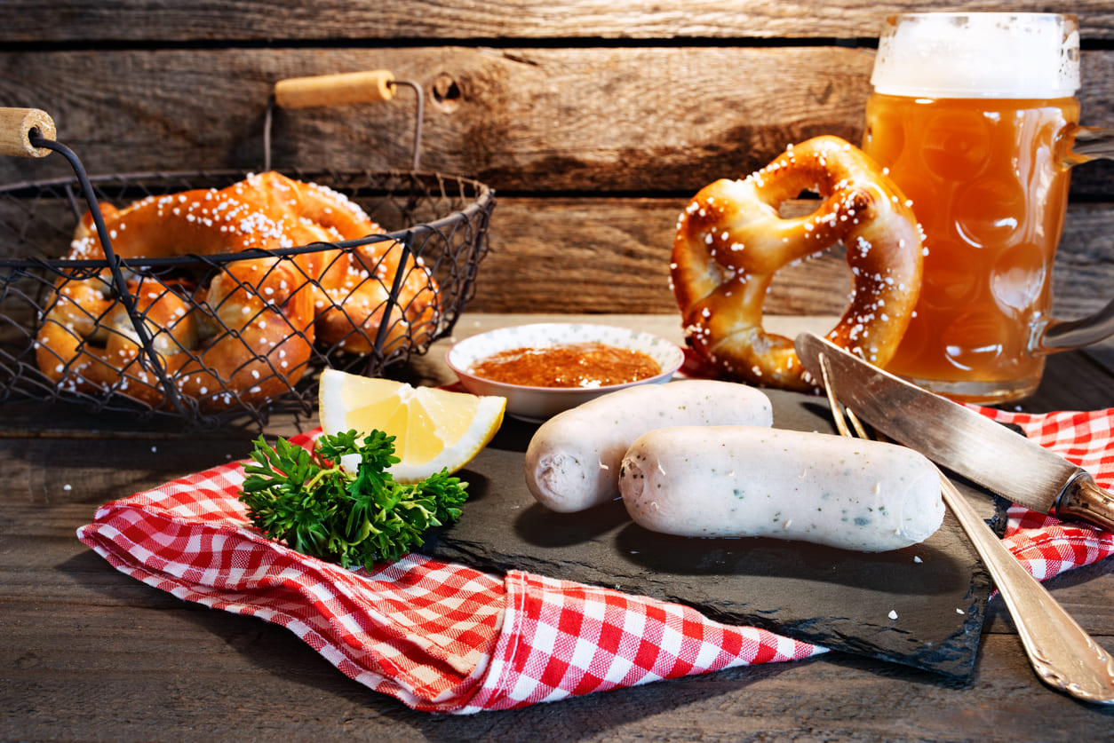 A classic Bavarian spread with pretzels, Weisswurst, mustard, and a frothy beer stein, evoking the spirit of German Beer Day.