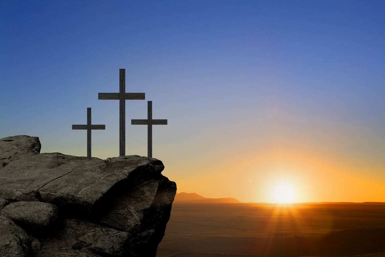 A serene sunrise illuminates three crosses atop a rocky hill, symbolizing reflection and hope.