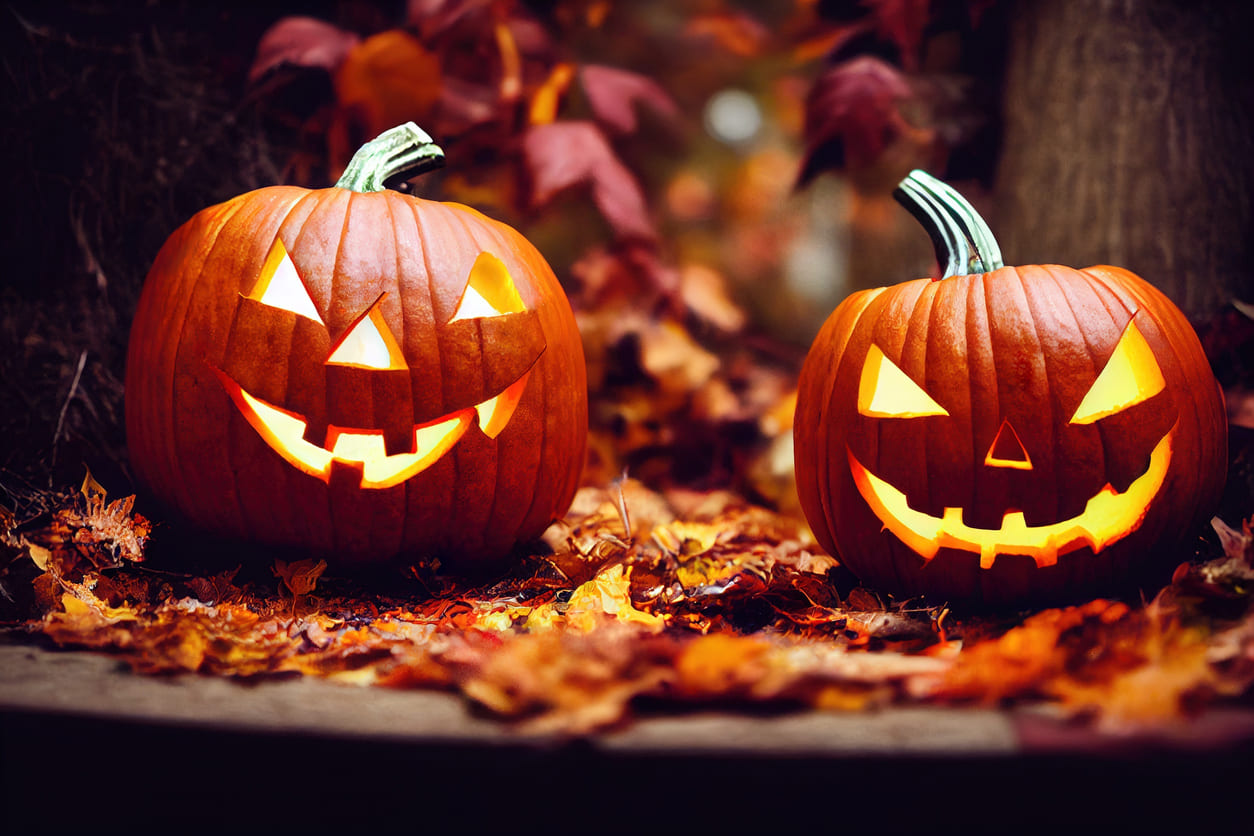 Two carved jack-o'-lantern pumpkins glowing warmly amidst autumn leaves, creating a festive Halloween atmosphere.