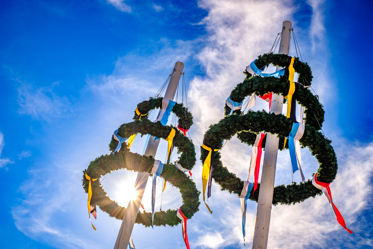 Maypoles decorated with vibrant wreaths and ribbons, symbolizing the festive spirit of May Day under a bright blue sky.