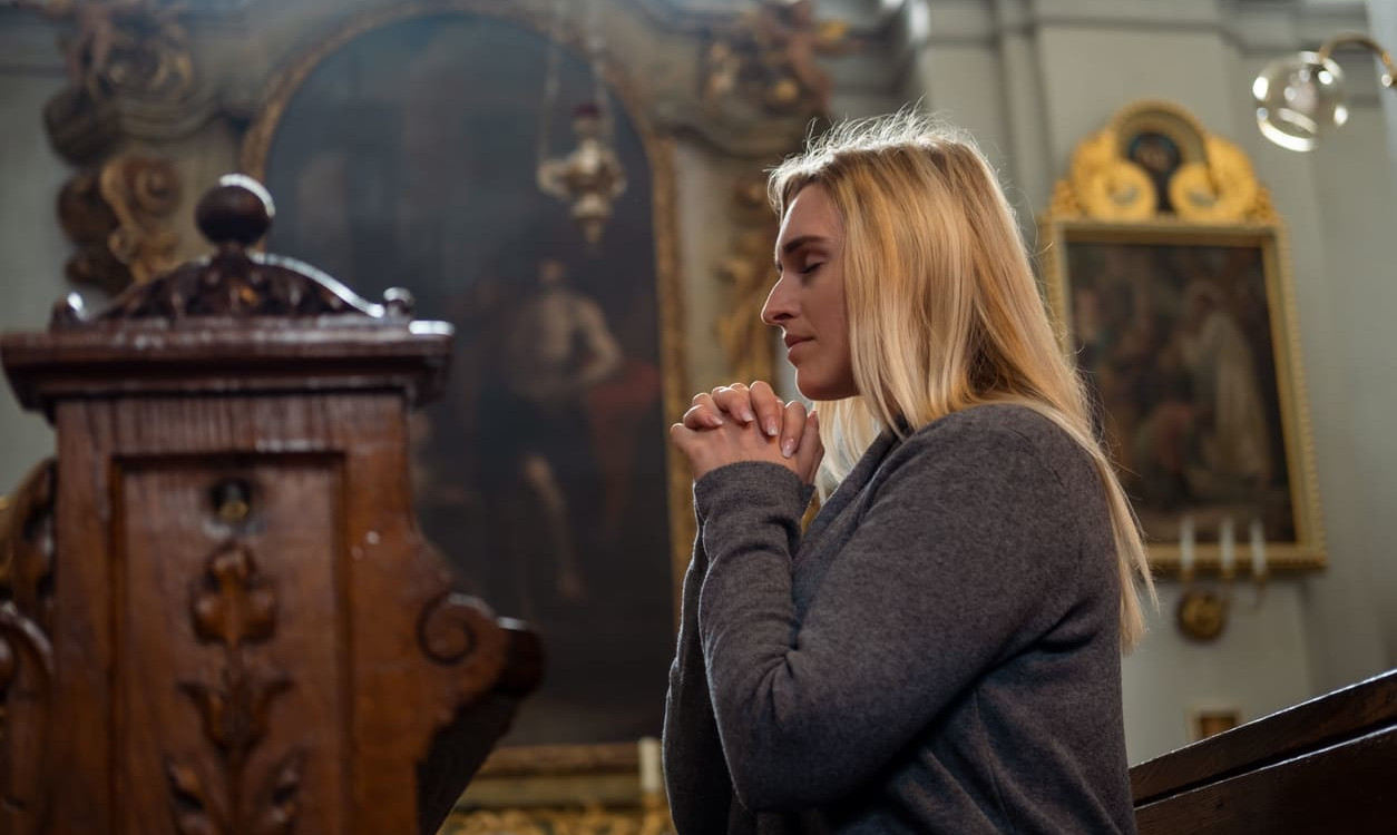 A woman prays thoughtfully in a serene church setting, surrounded by ornate religious decor.