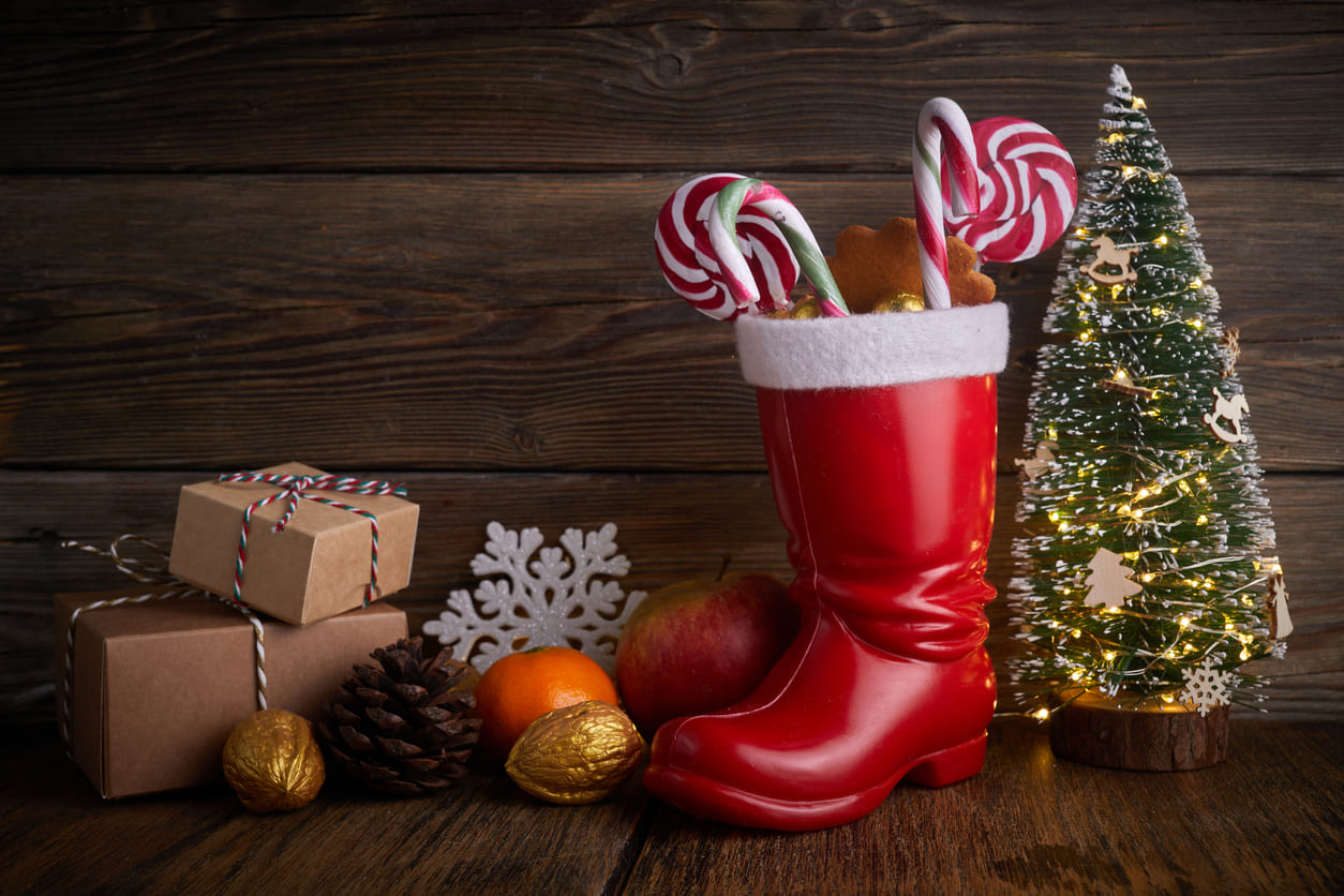 A red boot filled with candy canes, nuts, and fruits, surrounded by festive decorations, symbolizing Saint Nicholas Day traditions.