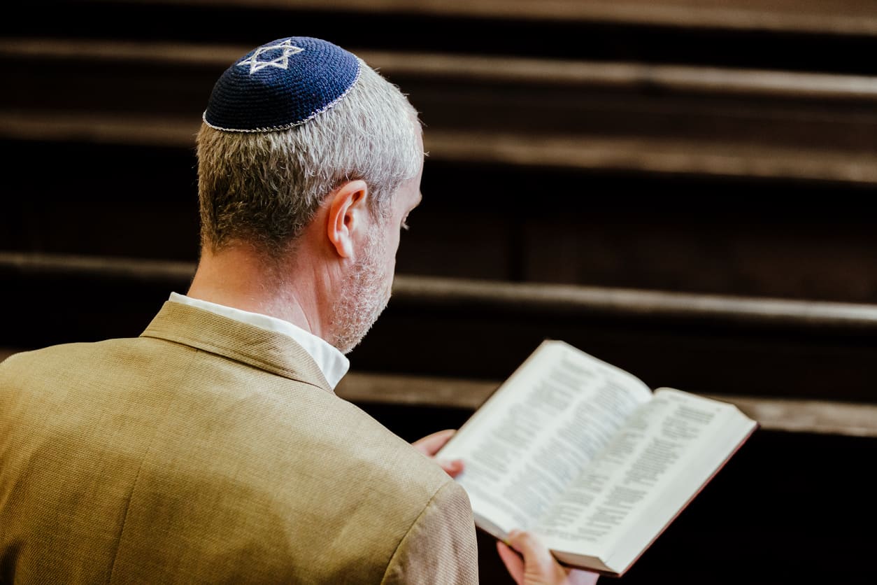 A man wearing a kippah, deeply engaged in prayer or reading sacred texts, symbolizing the reflective traditions of Rosh Hashanah.