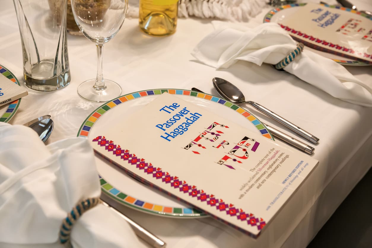 A Passover table set with colorful plates, utensils, and the Haggadah, symbolizing the traditions and significance of the Seder meal.