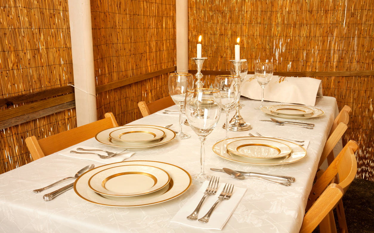 A festive dining table elegantly arranged inside a sukkah, ready for a Sukkot celebration.