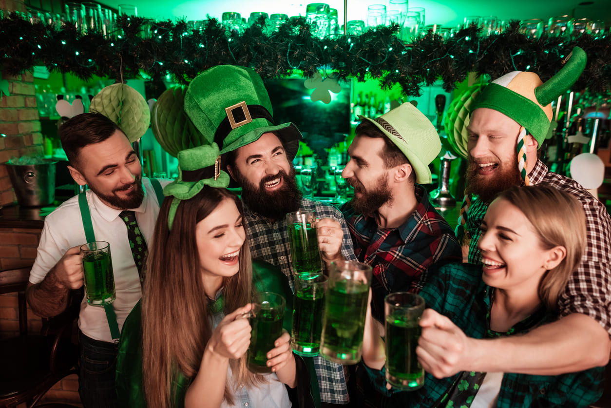 A lively group of friends dressed in green celebrates St. Patrick's Day with cheerful smiles and green drinks in a festive setting.