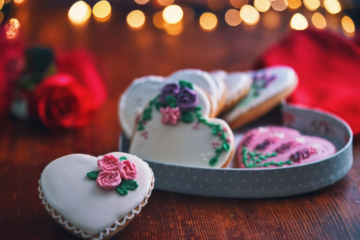 Heart-shaped cookies with floral designs, accompanied by a red rose and warm lights, evoking the romantic spirit of Valentine's Day.