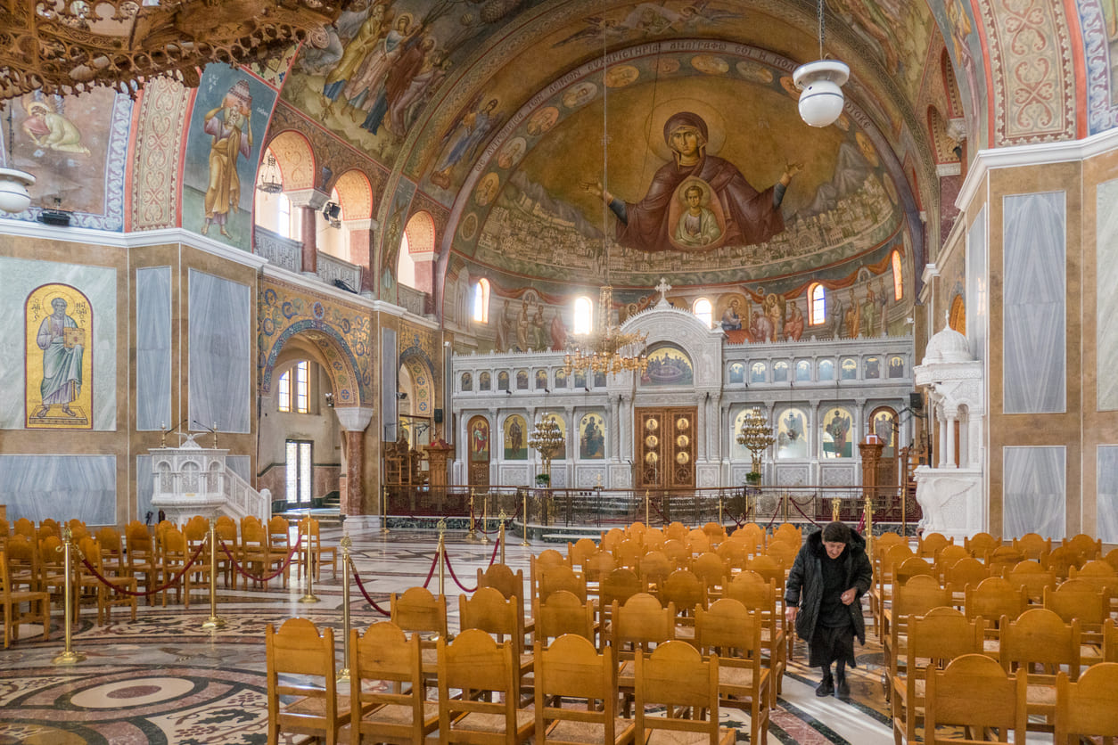 A serene Greek Orthodox church interior features a radiant icon of the Virgin Mary beneath the dome, capturing the solemn beauty of the Annunciation feast.