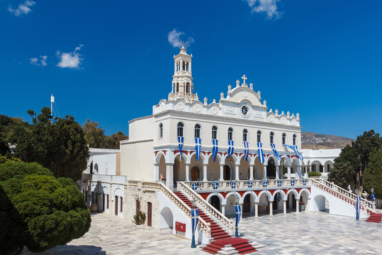 A grand view of the Church of Panagia Evangelistria in Tinos, adorned with flags and marble steps, welcoming pilgrims for the Dormition of the Holy Virgin.